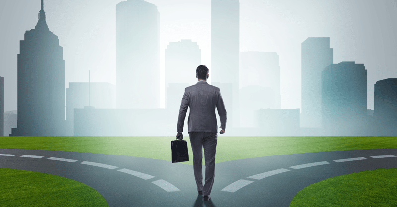 A man in a business suit holding a suitcase, standing at the split on the road, against a background of silhouetted buildings and skyscrapers