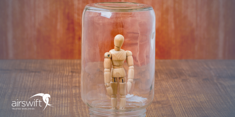 A wooden mannequin inside a clear jar on a wooden surface.