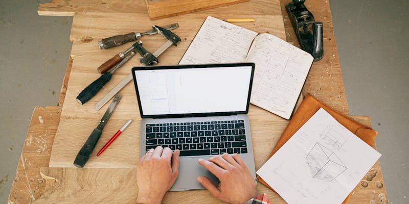 man working on a laptop in a workshop surrounded by tools