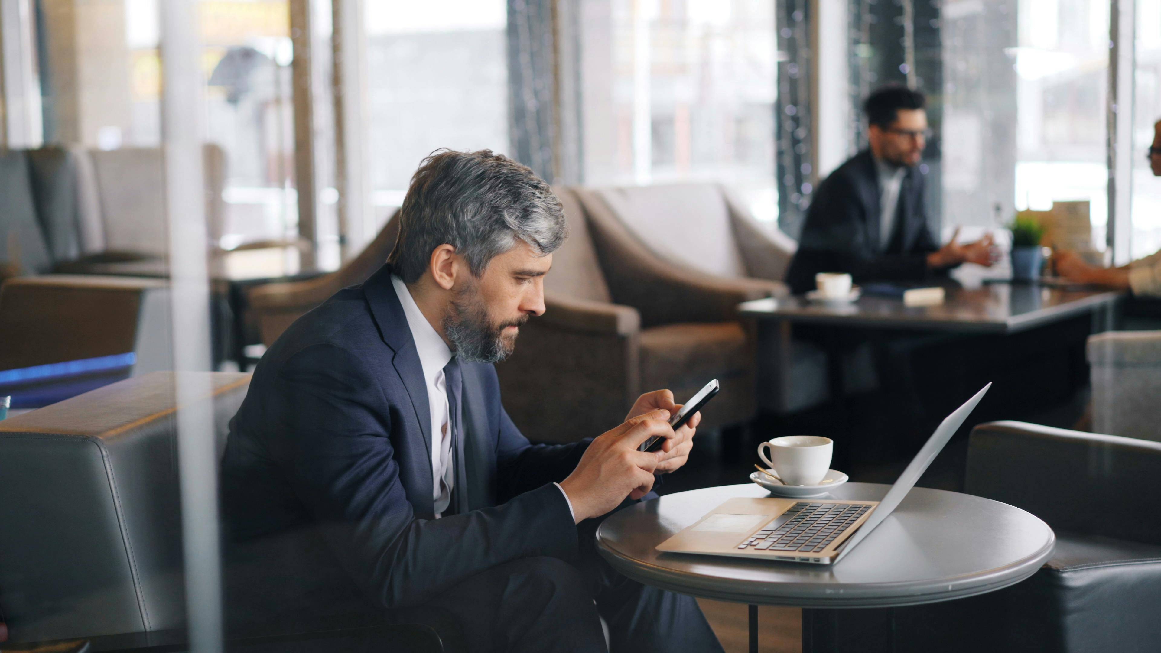 man in a co-working space checking emails on his phone and laptop